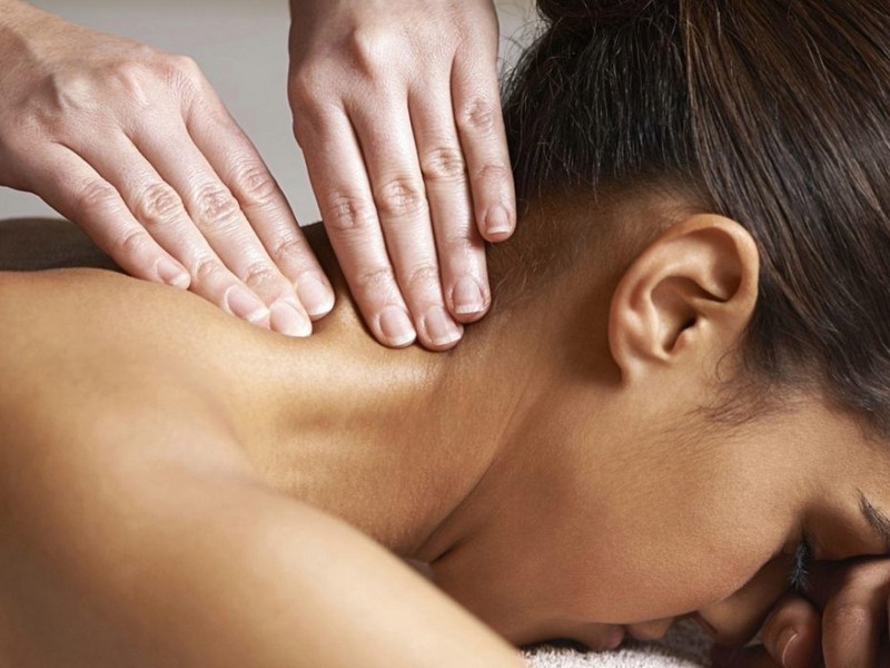 Person receiving a neck massage with their collar region exposed, therapist's hands applying pressure on the neck